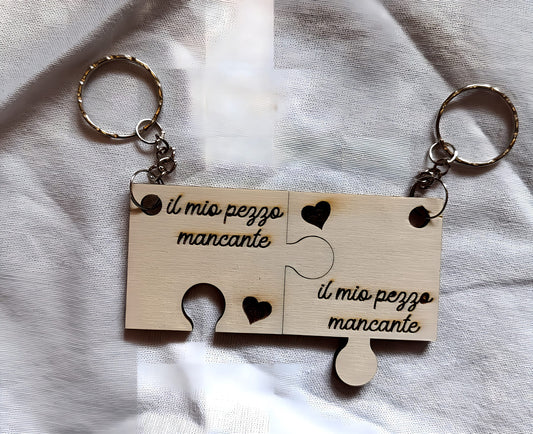 Wooden puzzle piece keychains with 'il mio pezzo mancante' engraved, heart cutouts, on fabric
