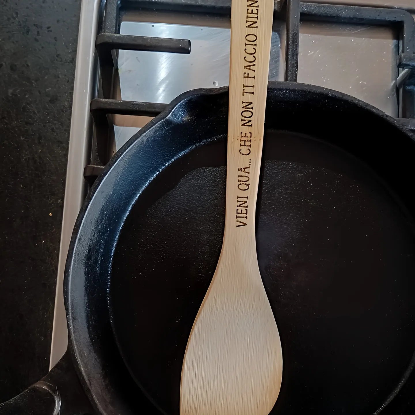 Wooden spoon with Italian engraving on cast iron pan over stove
