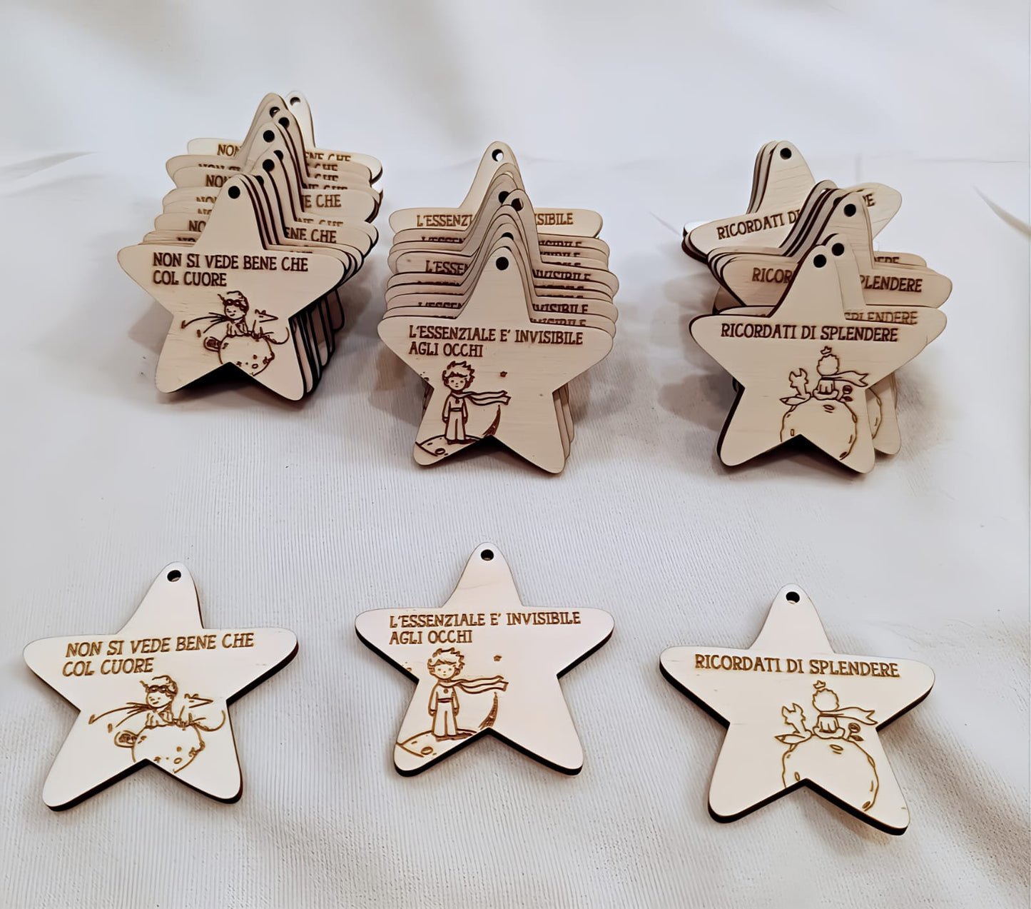 Wooden star-shaped ornaments with Italian quotes and Little Prince illustrations on white cloth.