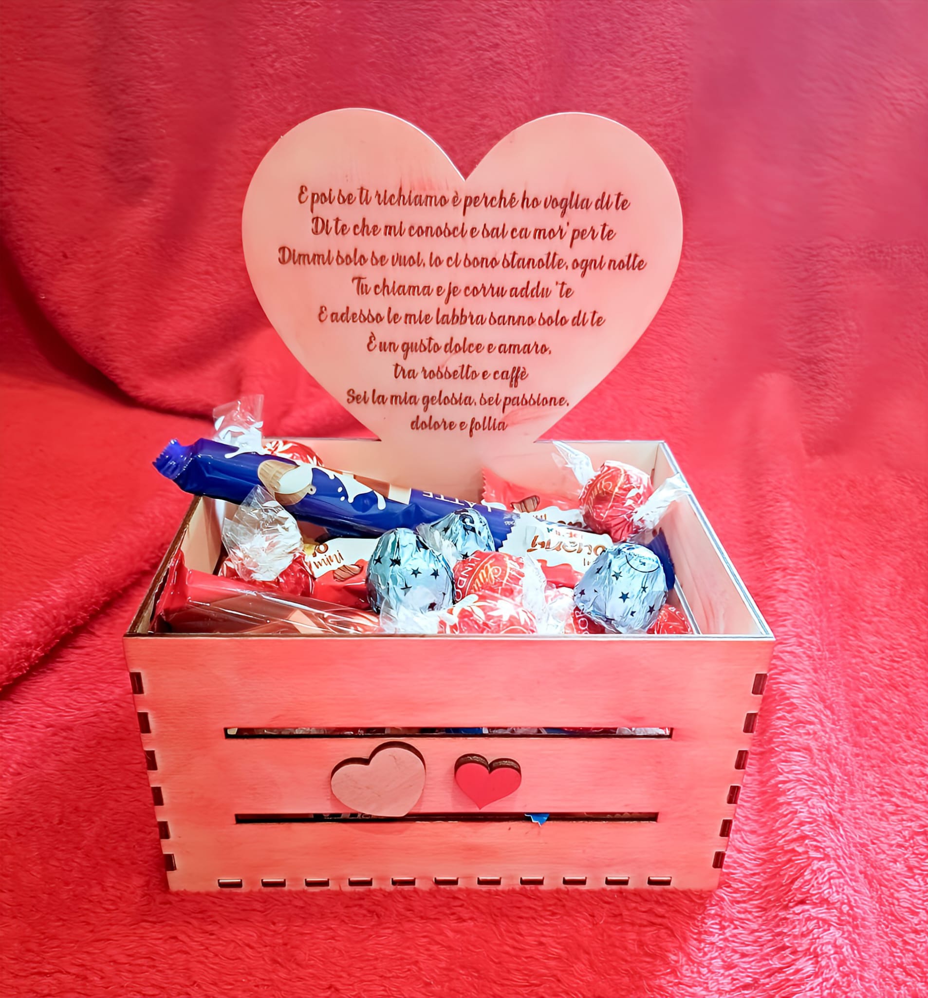 Pink wooden gift box with assorted chocolates and a heart-shaped card on a red fabric background