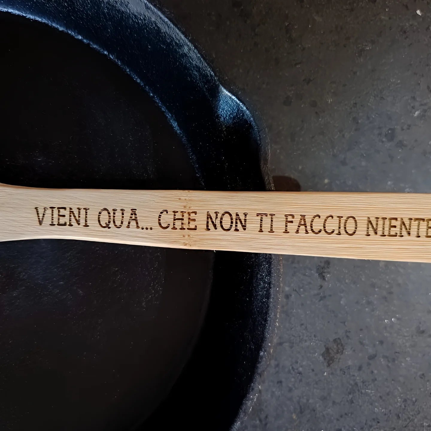 Wooden spoon with Italian phrase "VIENI QUA... CHE NON TI FACCIO NIENTE" beside cast iron pan